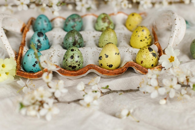 Happy Easter Stylish easter eggs and blooming spring flowers on rustic table Natural painted quail eggs in tray feathers and cherry blossoms linen fabric Rustic easter still life