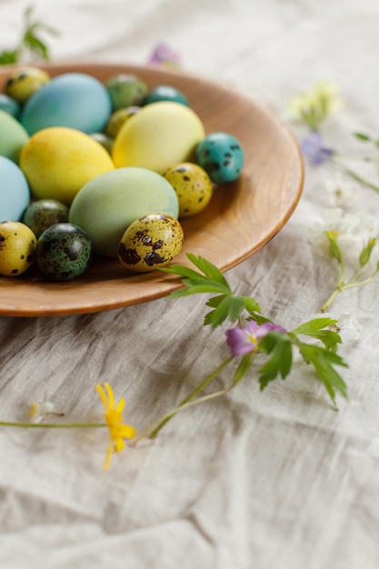 Happy Easter Stylish easter eggs and blooming spring flowers in wooden bowl on rustic table Natural painted eggs and blossoms on linen fabric Rustic easter still life