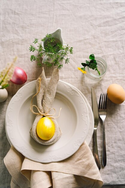 Happy Easter Stylish easter eggs on a napkin with spring flowers on white wooden background Table setting The concept of a happy Easter holiday