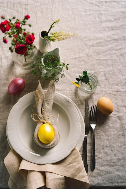 Happy Easter Stylish easter eggs on a napkin with spring flowers on white wooden background Table setting The concept of a happy Easter holiday