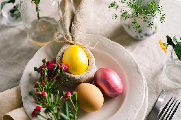 Happy Easter Stylish easter eggs on a napkin with spring flowers on white wooden background Table setting The concept of a happy Easter holiday