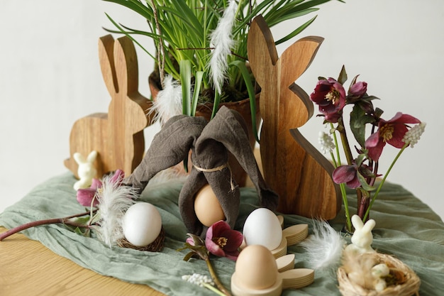 Photo happy easter stylish wooden bunny spring flowers natural eggs and napkin bunny ears on rustic table in room easter still life festive arrangement and decor in farmhouse