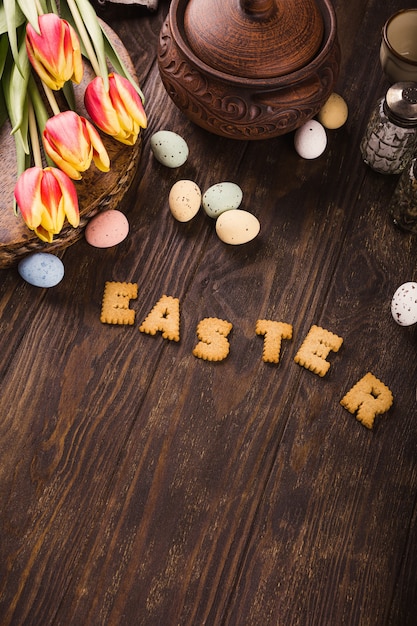 Happy Easter surface, Lettering from cookies, tulips and colorful quail eggs in metal basket on wooden surface