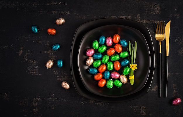 Happy Easter Table setting for Easter holiday Easter chocolate eggs and cutlery on dark background Top view flat lay