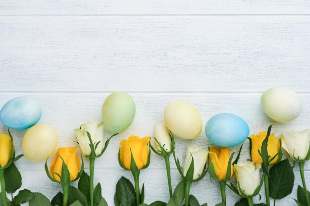 Happy Easter Yellow and white roses and colored eggs on white wooden background Easter background with copy space Floral pattern Greeting card Mock up Space for text