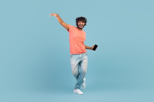 Happy eastern guy using wireless headset and smartphone dancing