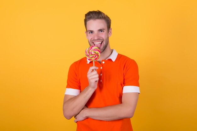 Happy eating sweets Symbol of happiness Man eat lollipop Man smiling hold lollipop Holiday concept Sugar harmful for health Guy lollipop candy yellow background Sweet boy Taste of childhood