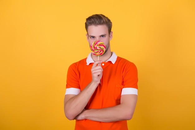 Happy eating sweets. Symbol of happiness. Sweet boy. Taste of childhood. Man eat lollipop. Man smiling hold lollipop. Holiday concept. Sugar harmful for health. Guy lollipop candy yellow background.