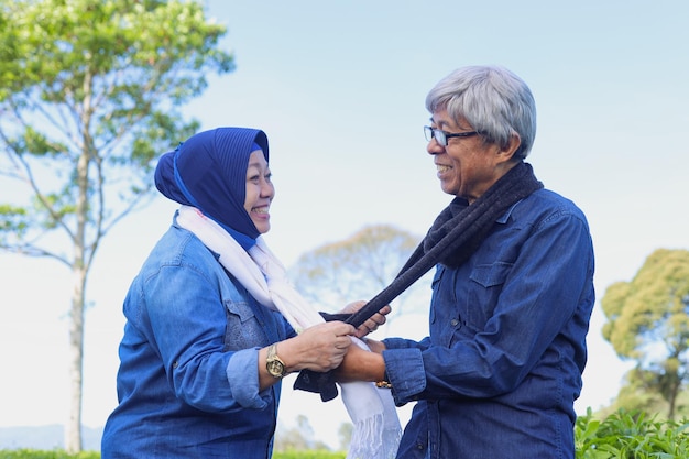 Happy elderly couple laughing and holding each other's scarf at tea plantation