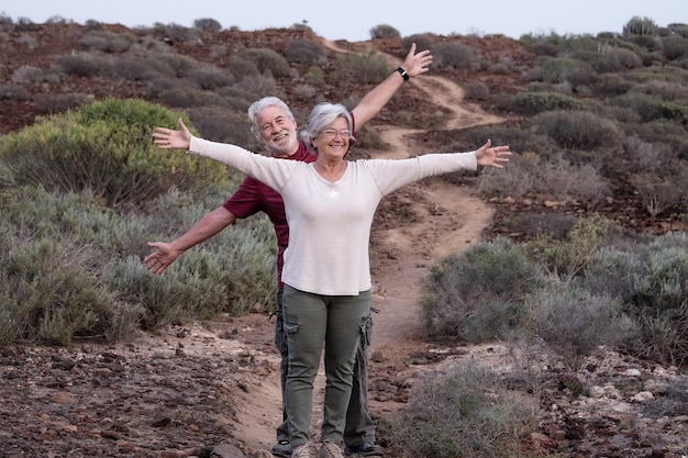 Happy elderly couple with outstretched arms enjoying outdoors excursion, sunset light