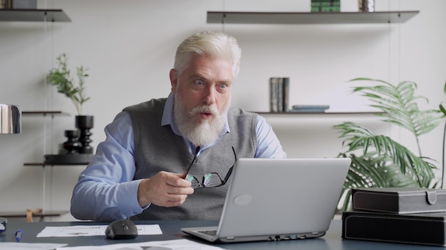 Happy an elderly man with a gray beard completed task and triumphing with raised hands