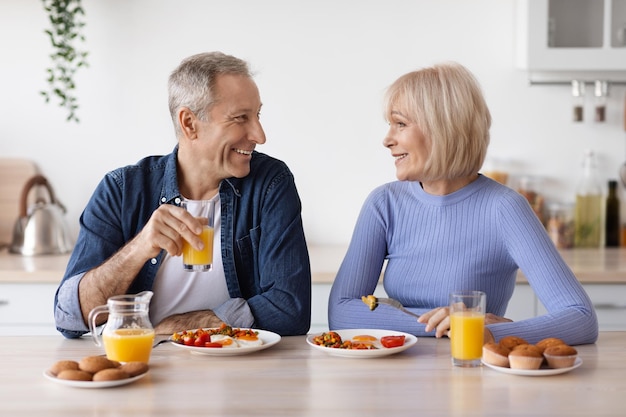 Happy elderly man and woman having breakfast at home chatting