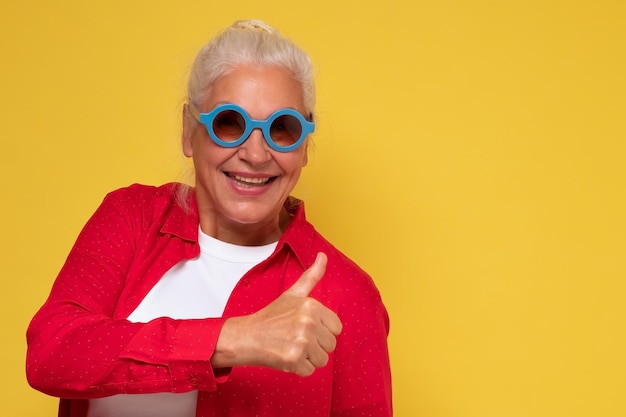 Happy elderly woman wearring sunglasses holding her thumb up