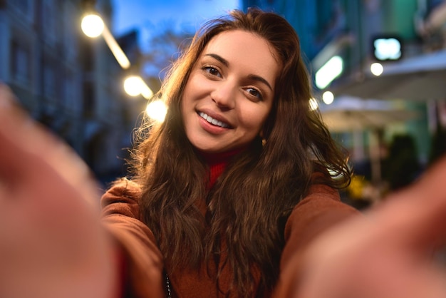 Photo happy elegant young woman in red coat taking selfies while walking around the city woman hugs her boyfriend