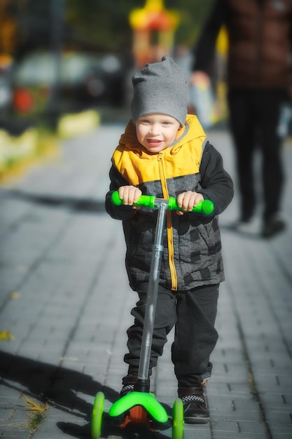 Happy and emotional toddler rides a threewheeled scooter in the park along the path