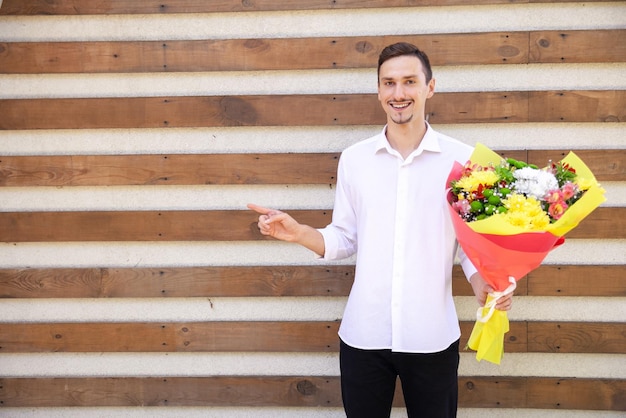 Happy European guy in a white shirt and black jeans holding a large bouquet of flowers