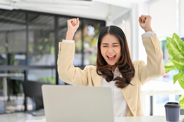 Happy and excited Asian businesswoman looking at laptop screen screaming with happiness