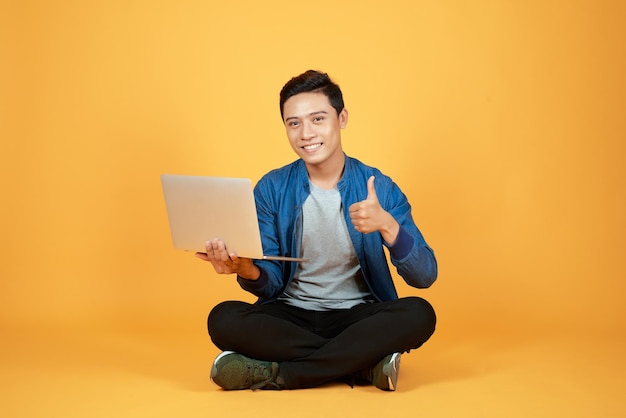 Happy excited Asian man holding laptop and raising his arm up to celebrate success or achievement