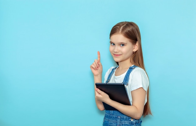 A happy excited girl points her finger up at the copy space standing isolated