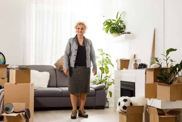 Happy excited mature retired middle aged woman standing in modern living room interior alone with arms outstretched enjoy freedom and wellbeing feel motivated at new furnished renovated home concept