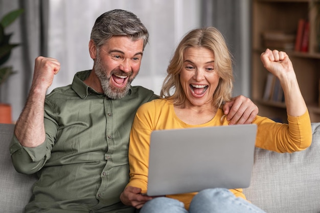 Happy Excited Middle Aged Spouses Celebrating Success With Laptop At Home