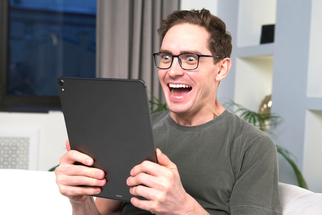 Happy excited wondered crazy man, happy successful guy winner looking at screen of tablet computer