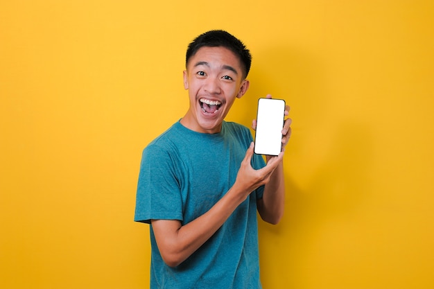 Happy Excited Young Asian man shock showing white phone screen at camera, isolated on yellow background