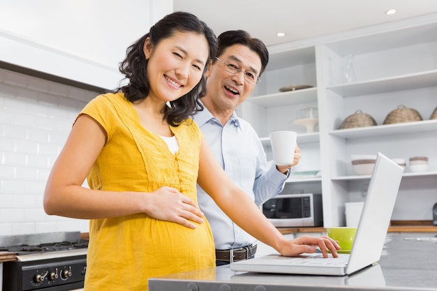 Happy expectant couple using laptop in the kitchen