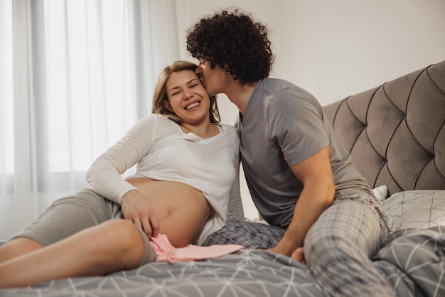 Happy expecting couple in love enjoying while relaxing on a bed in bedroom.