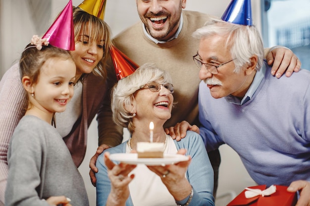 Happy extended family having fun while celebrating Birthday at home Focus is on mature woman holding Birthday cake