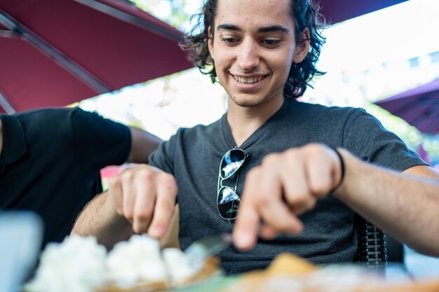 Happy face of a man cutting a crepe with cream on the terrace of a restaurant next to other people