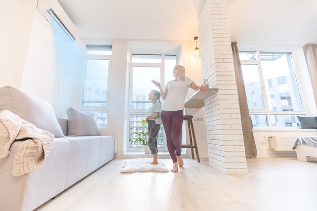 Happy family under air conditioner, mom holding remote control switch on conditioning in living room adjust comfort temperature for daughter, climate system at modern home