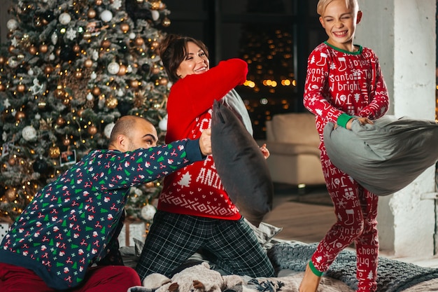 Happy family on the bed near the Christmas tree play pillow