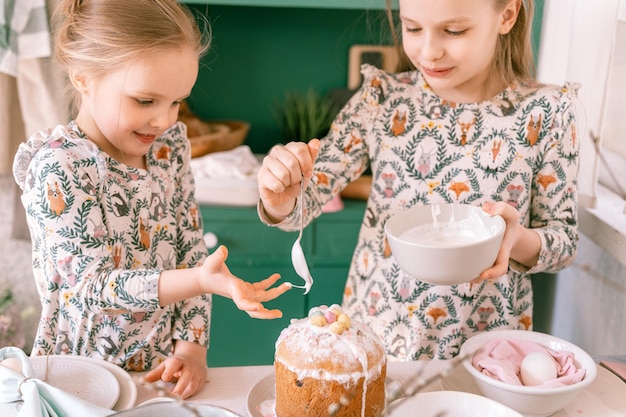 Happy family candid little kids sisters girls together have fun ready springtime Easter holiday at home in kitchen decorating table and Easter cakes bakery sweet icing and candy for lunch or dinner