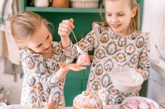 Happy family candid little kids sisters girls together have fun ready springtime Easter holiday at home in kitchen decorating table and Easter cakes bakery sweet icing and candy for lunch or dinner