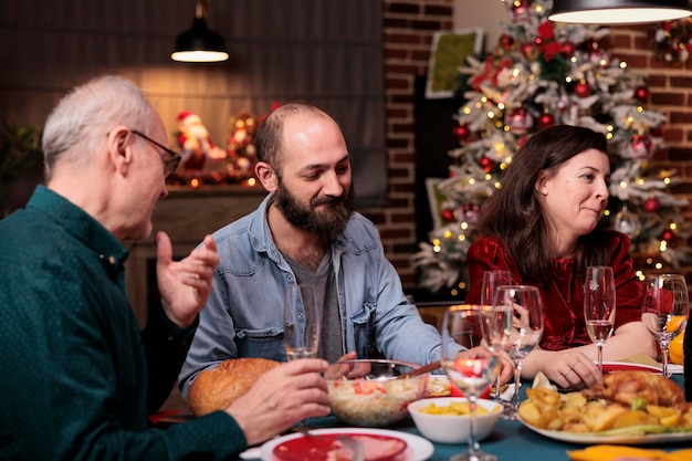 Happy family celebrating christmas, people talking at festive dinner table, eating traditional winter holiday food, chatting. Xmas eve celebration with parents at home party