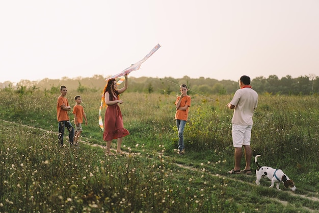 Happy family and children run on meadow with a kite in the summer on the nature Family playing with kite while running along rural summer field Family day