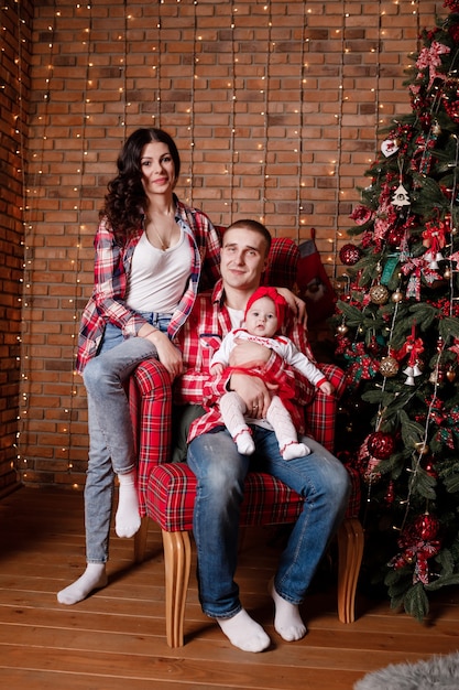 Happy family at Christmas eve sitting together near decorated tree at living room home Father mother and baby girl Concept of celebrating New Year holiday