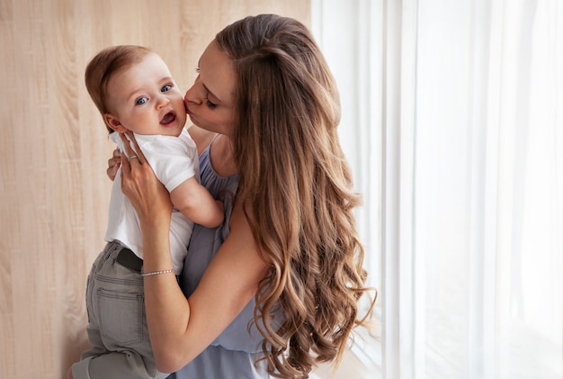 Happy family. Close up portrait of young attractive mother holding baby in her arms and gently kissing son