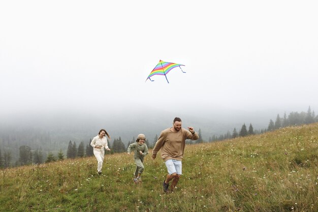 Happy family concept. parents and child are playing with a colorful kite. Young mother, father and little cute daughter having fun together outdoors in foggy day.