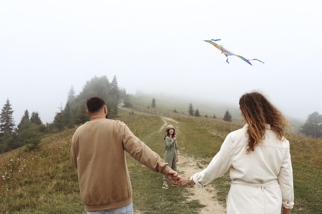 Happy family concept. parents and child are playing with a colorful kite. Young mother, father and little cute daughter having fun together outdoors in foggy day.