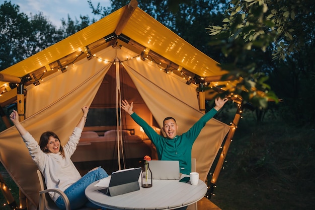 Happy family couple freelancers working laptop on a cozy glamping tent in summer evening Luxury camping tent for outdoor holiday and vacation Lifestyle concept