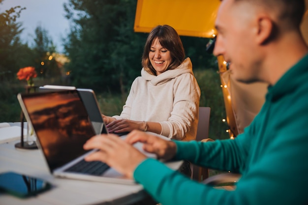 Happy family couple freelancers working laptop on a cozy glamping tent in summer evening Luxury camping tent for outdoor holiday and vacation Lifestyle concept