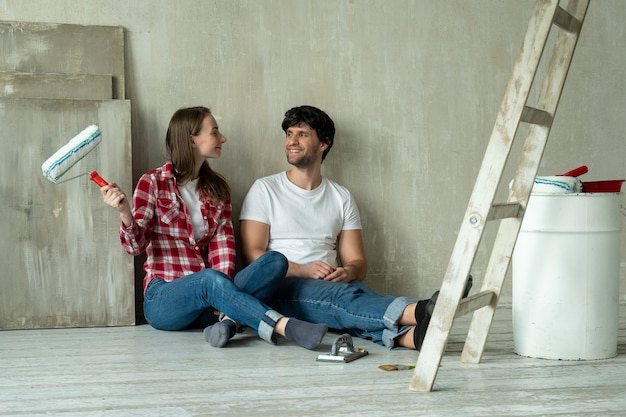 Happy family couple relaxing after painting young couple lying on the floor of new house and communicate with each other