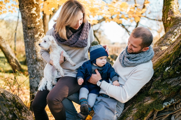 Happy family couple with their little child  and puppy spending time in autumn park.