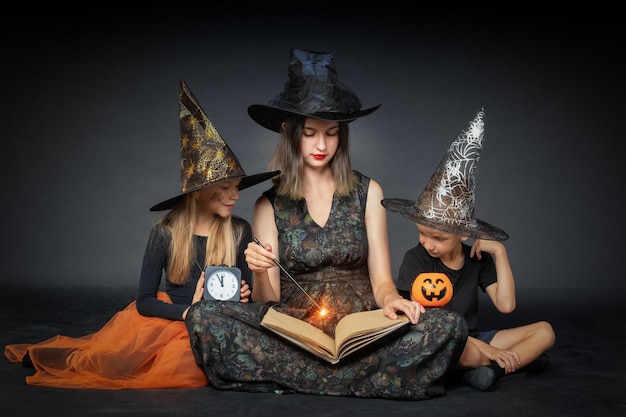 A happy family in creepy costumes of witches and wizards holding a large book with predictions and a magic wand