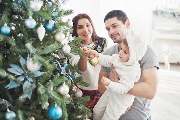 Happy Family Decorating Christmas Tree together. Father, Mother And Daughter. Cute Child