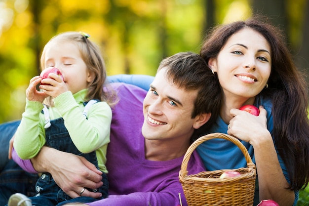 Happy family eating apples in autumn park