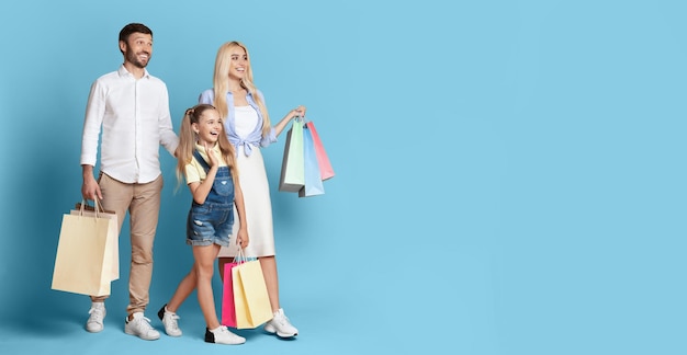 Happy Family Enjoying Shopping With Bags In Hand Against Blue