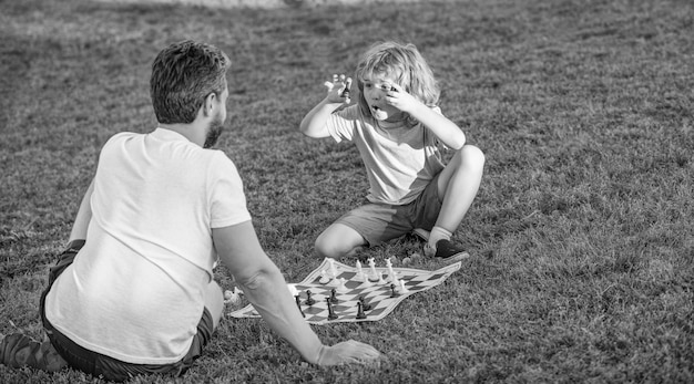 Happy family of father man and son kid playing chess on green grass in park outdoor education